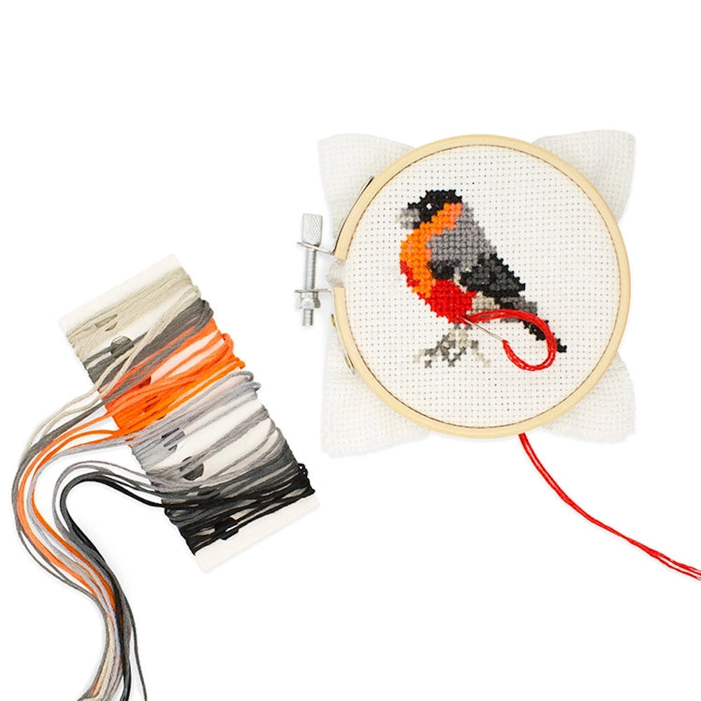 Bird mini cross stitch kit with a bullfinch in a wooden hoop and colorful embroidery thread on a white background.