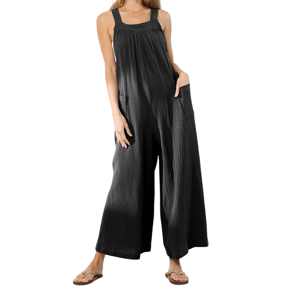 A woman wearing a loose, textured black jumpsuit with wide legs and side pockets, paired with sandals.