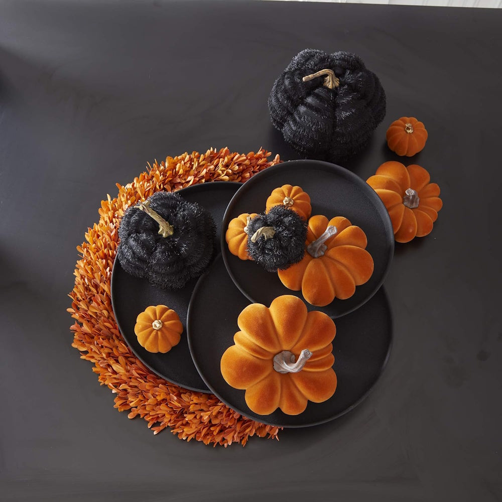 Black textured fabric pumpkins and velvet orange decorative pumpkins arranged on dark plates with an orange wreath.