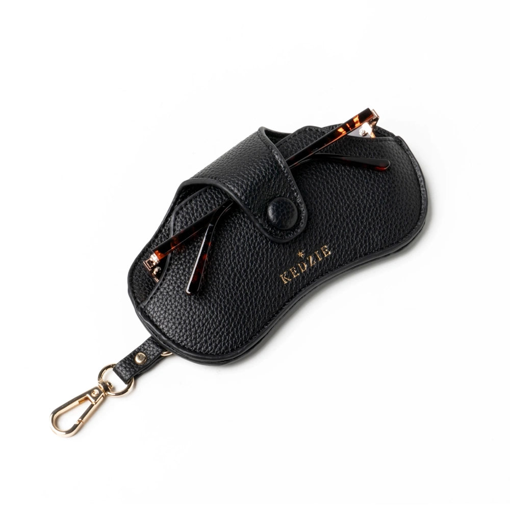 Black pebbled leather Kedzie eclipse eyewear case with gold hardware, holding tortoiseshell sunglasses on a white background.