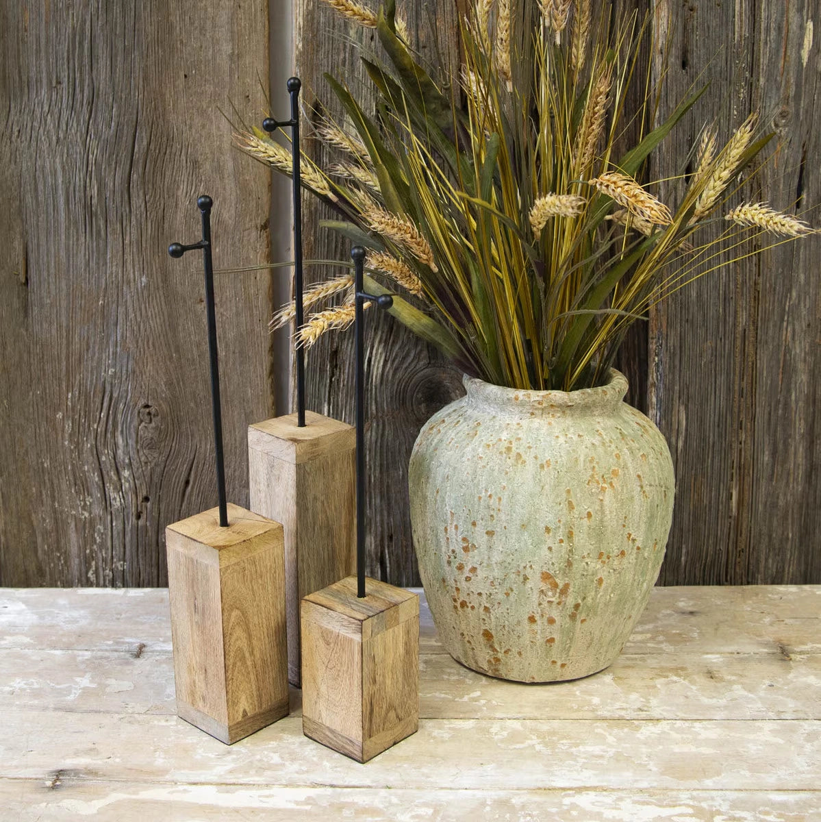 Front view of three natural wood and black metal charm display stakes on a rustic table.