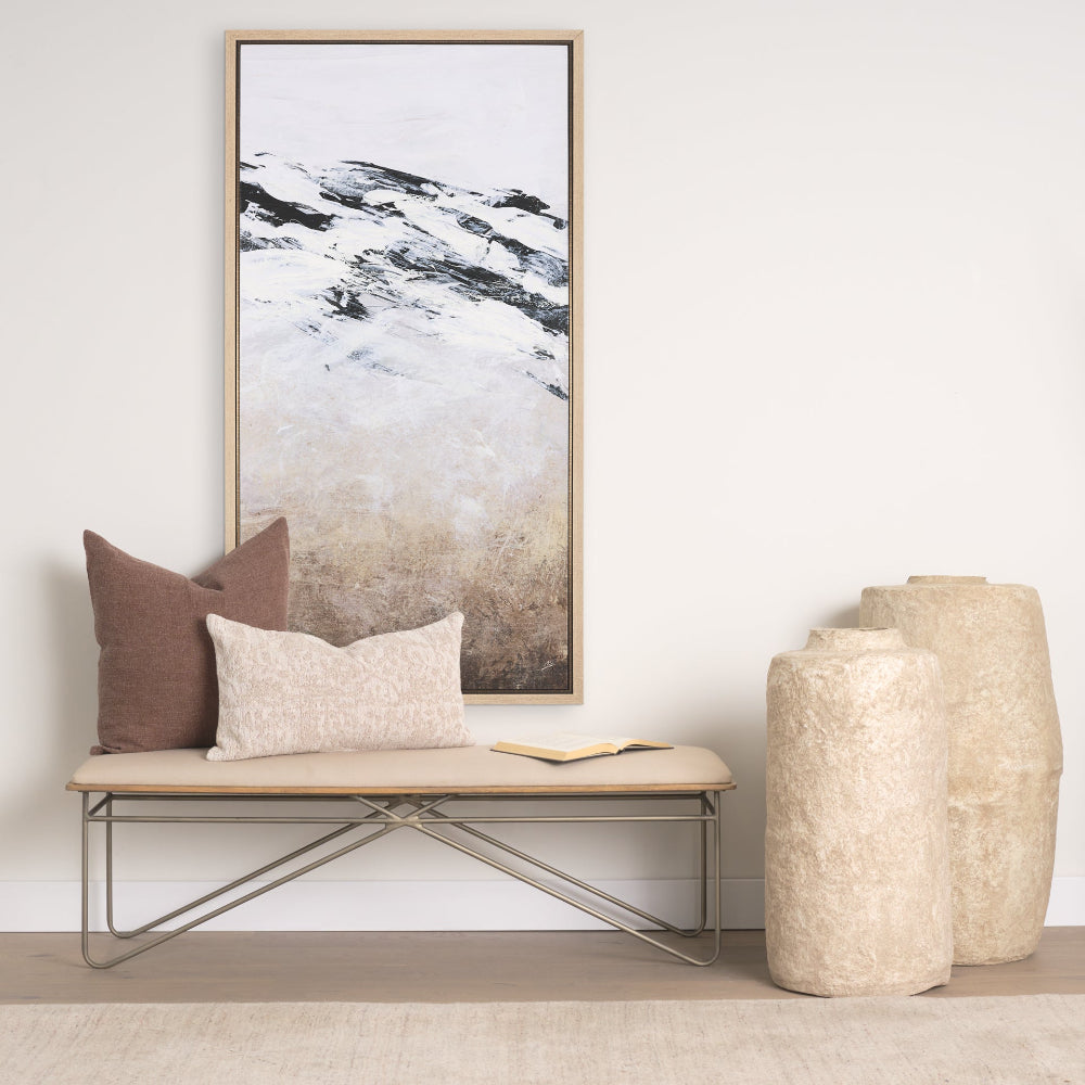 Framed abstract canvas hung above a cushioned bench with pillows, beside two tall textured vases.