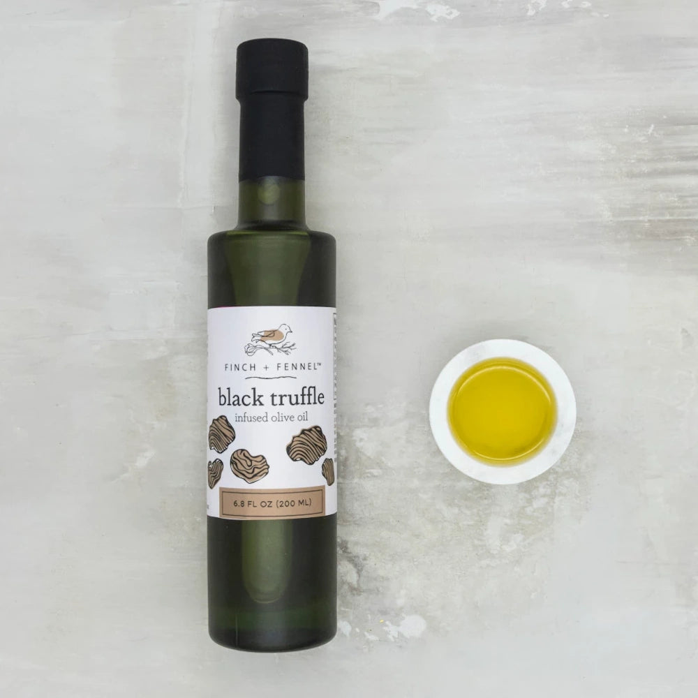 Bottle of Finch + Fennel black truffle infused olive oil next to a small bowl of golden oil on a gray surface.
