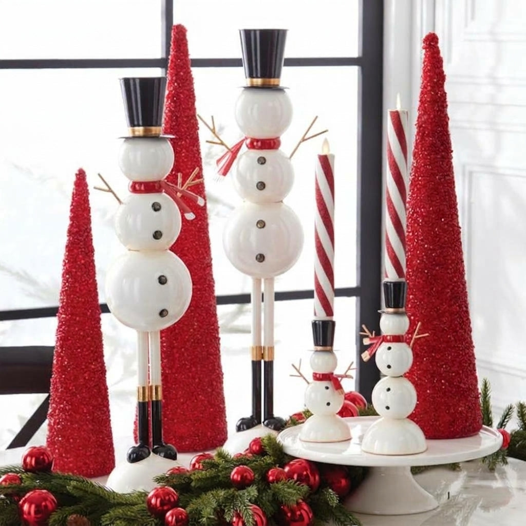 Lifestyle display of the white metal snowman taper candleholders alongside red glitter cone trees and festive greenery.