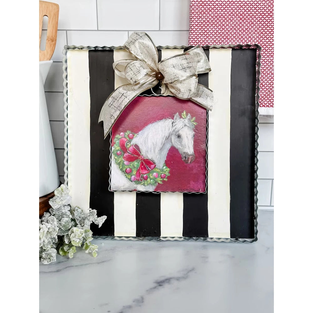Christmas horse art display board with a silver bow and holiday greenery on a marble countertop.