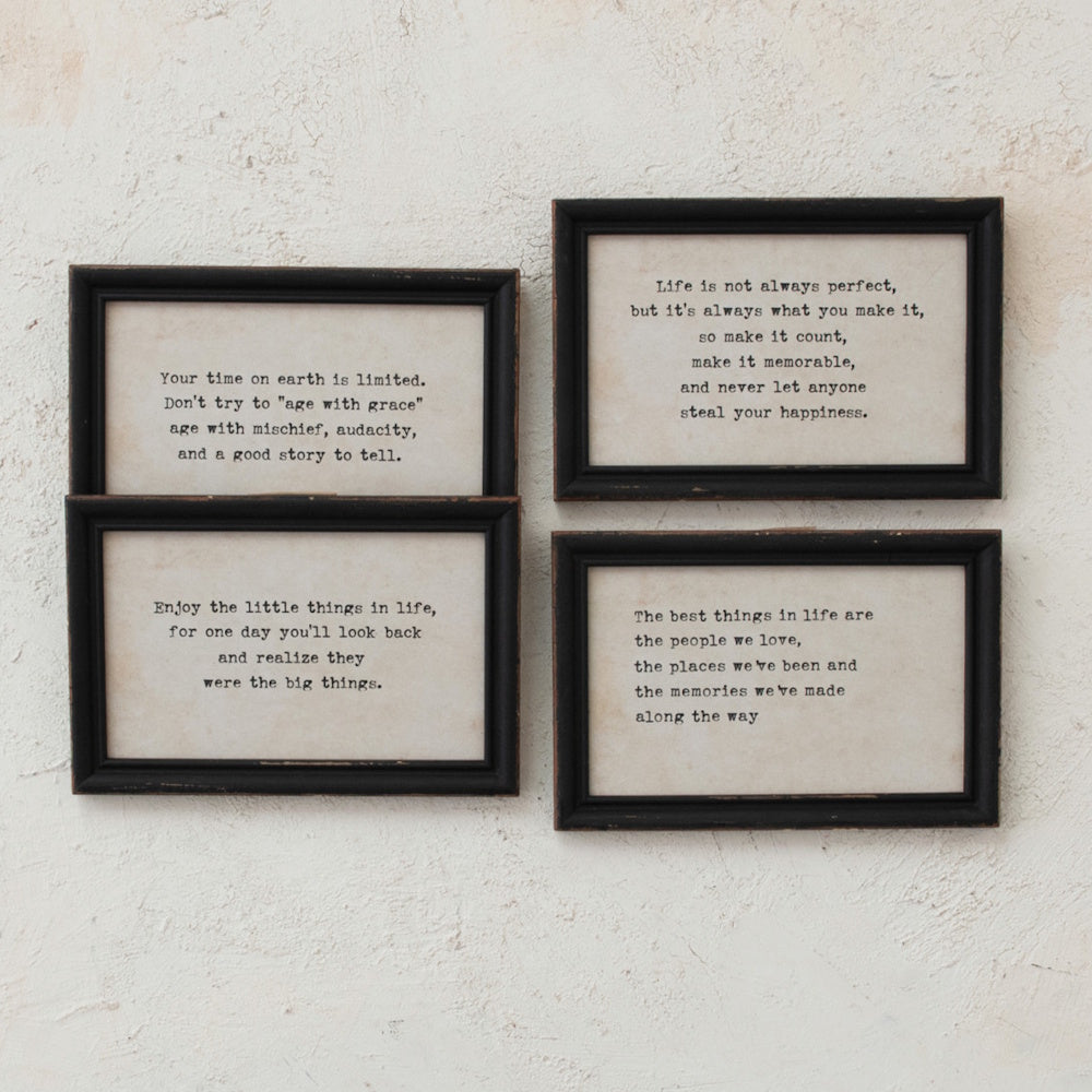 Four rectangular black-framed wall decor pieces with printed inspirational quotes on a textured wall.