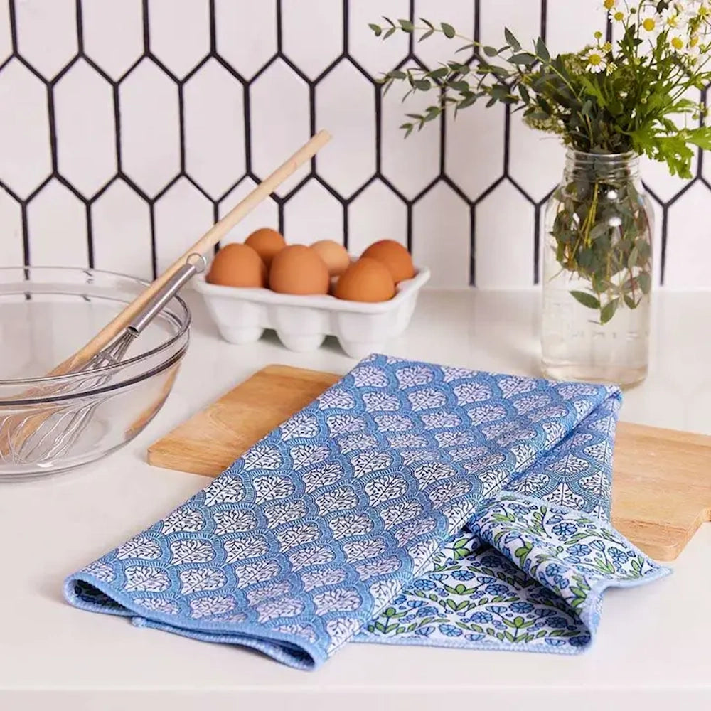 Blaire Blue eco-friendly tea towel with a blue floral pattern on a kitchen counter near eggs, a bowl, and flowers.