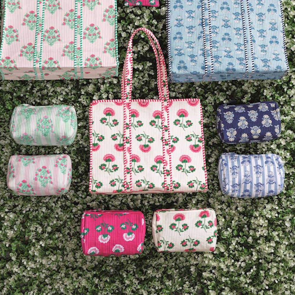 Assorted block-print tote bags and matching cosmetic pouches in various floral patterns on a green hedge background.