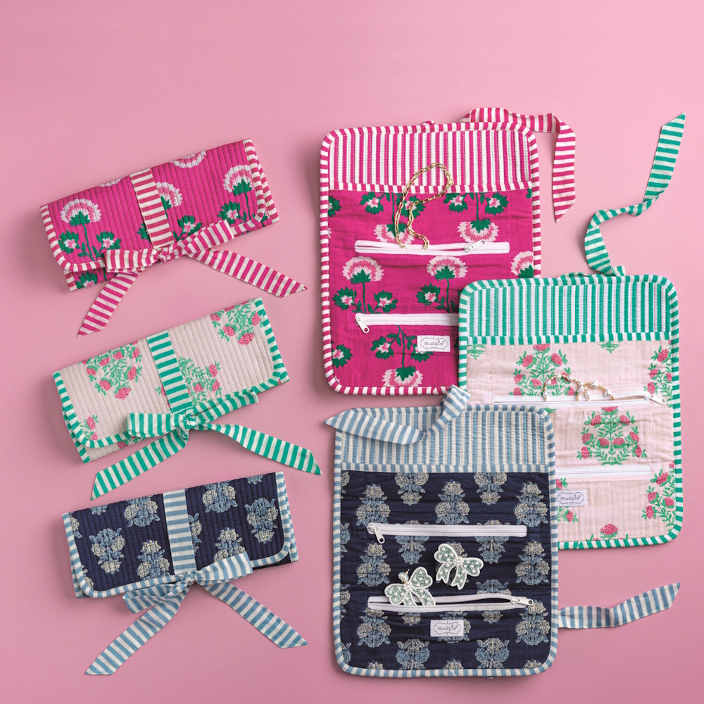 Floral and striped block-print fabric jewelry rolls in pink, cream, and navy shown open and closed on a pink background.