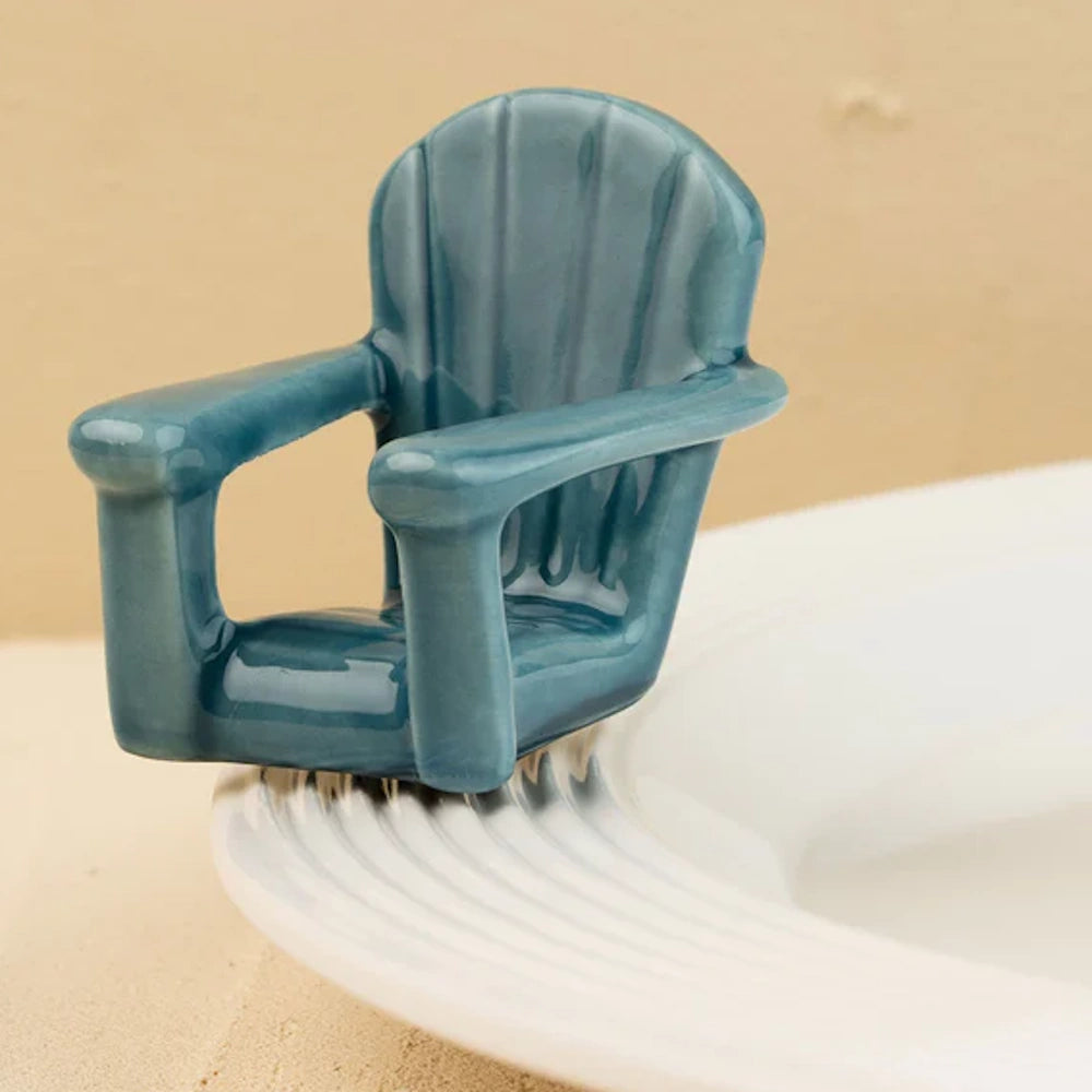 A miniature glossy blue ceramic Adirondack chair sitting on the edge of a white textured plate.