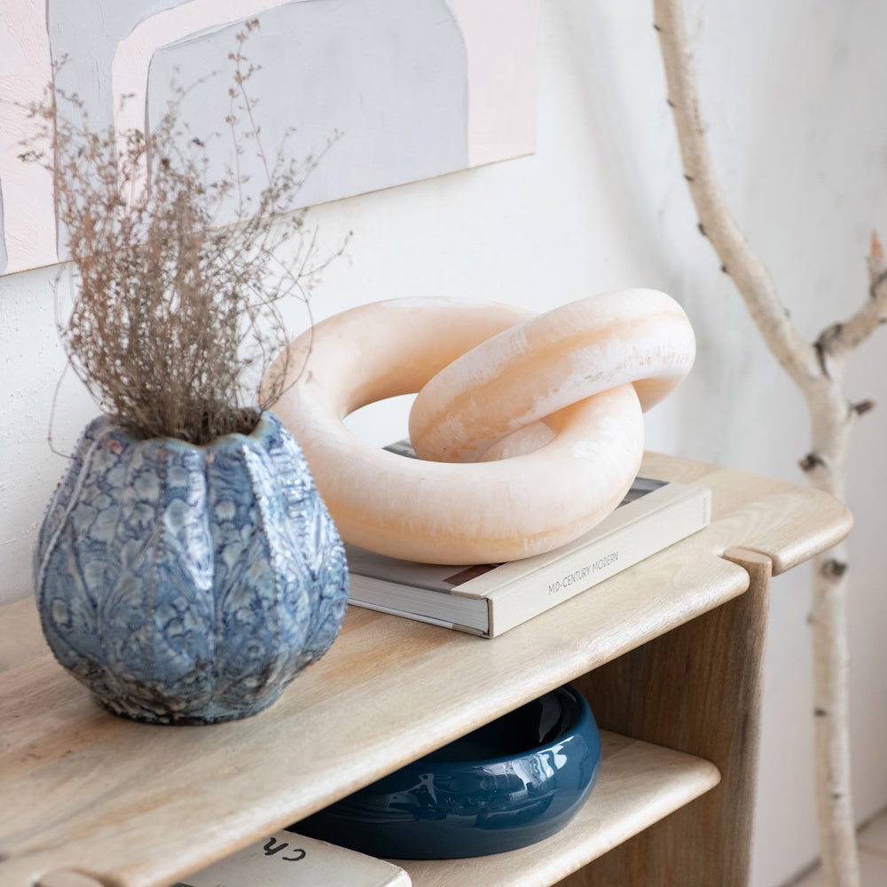 Blue embossed stoneware vase with dried sprigs next to a marble chain link sculpture.