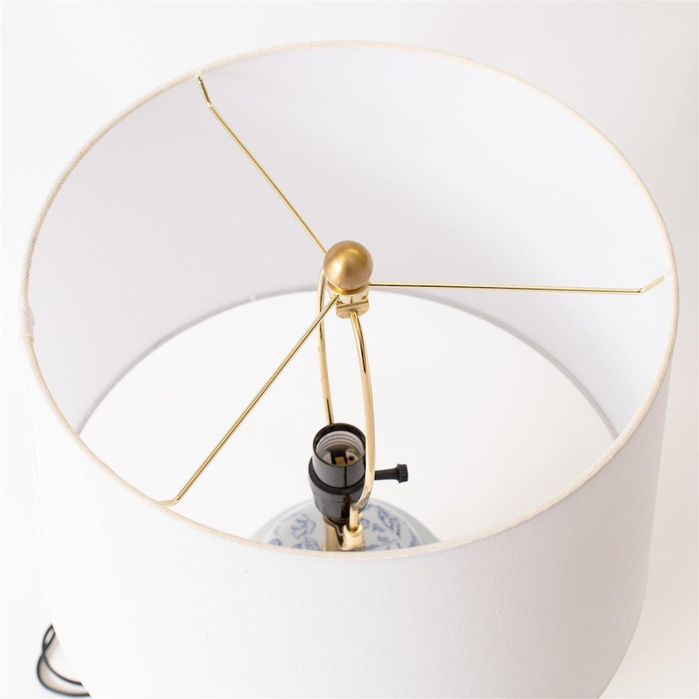 Top view of a blue floral ginger jar lamp with a white drum shade, brass harp, and gold finial on a white background.