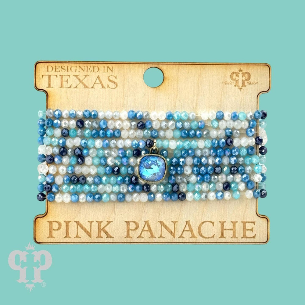 A set of blue and white beaded bracelets with a central blue gemstone charm, displayed on a wooden card.