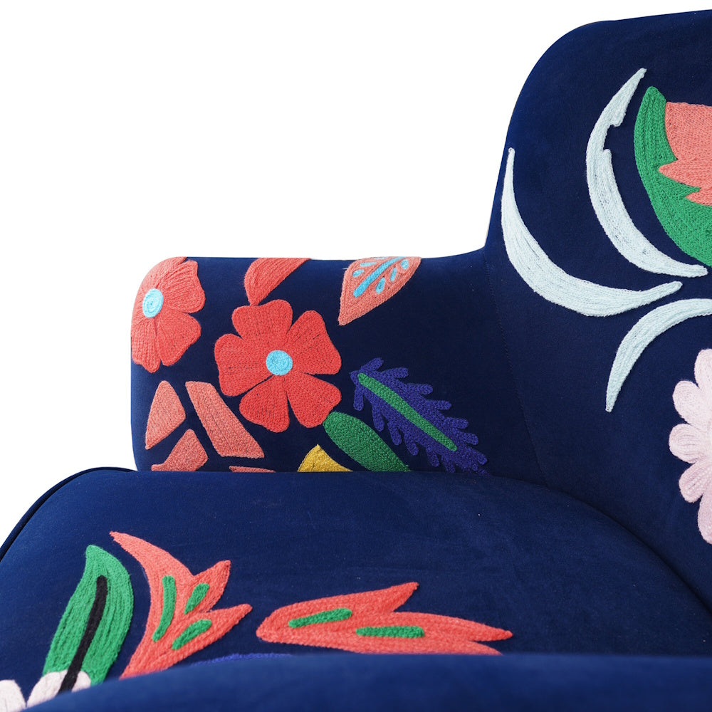 Close up of navy blue accent chair arm and seat with vibrant floral embroidery and detailed stitched patterns.
