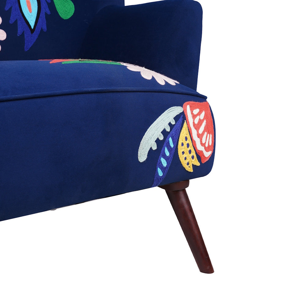 Close up of navy blue accent chair base with colorful floral embroidery and angled wooden leg detail.