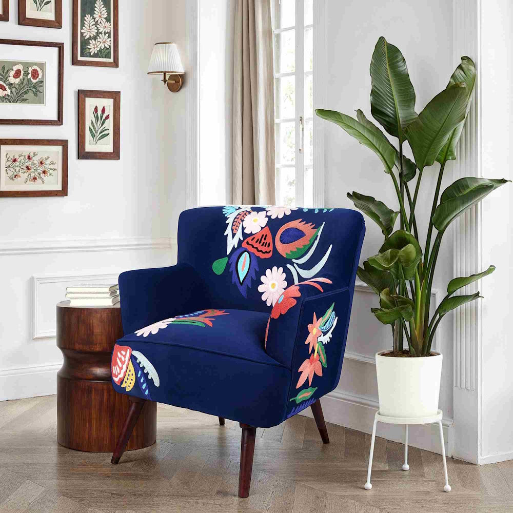 Navy blue floral accent chair styled in a bright living room with botanical wall art and indoor plant.