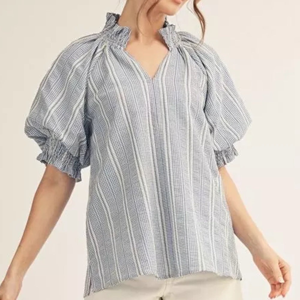 Woman wearing a blue and white gingham blouse with puff sleeves, a ruffled collar, and a V-neckline.