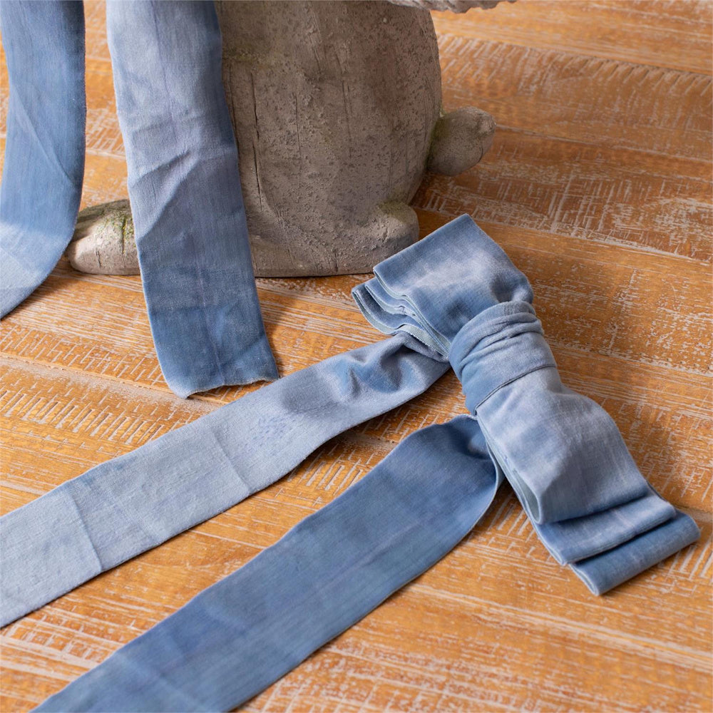 Dusty blue velvet ribbon bow on rustic wood background with stone statue base. High-quality craft textile.