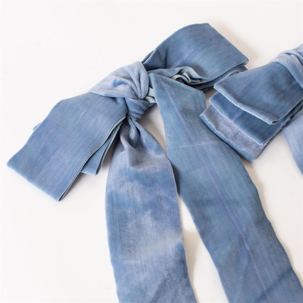 Hand-tied dusty blue velvet ribbon bow with long tails, isolated on a white background for wedding and gift decor.