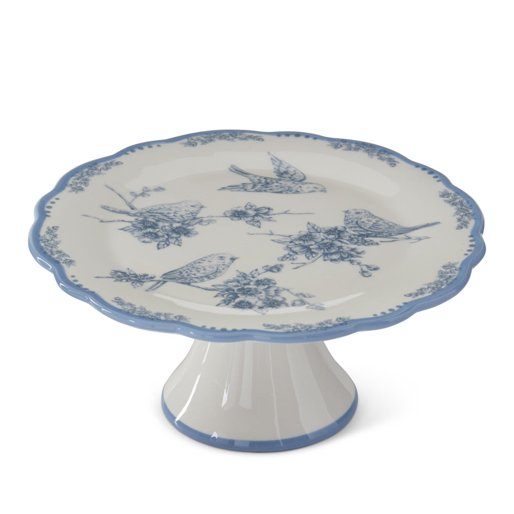 White and blue ceramic cake stand featuring a floral and bird pattern with a scalloped edge on a white background.