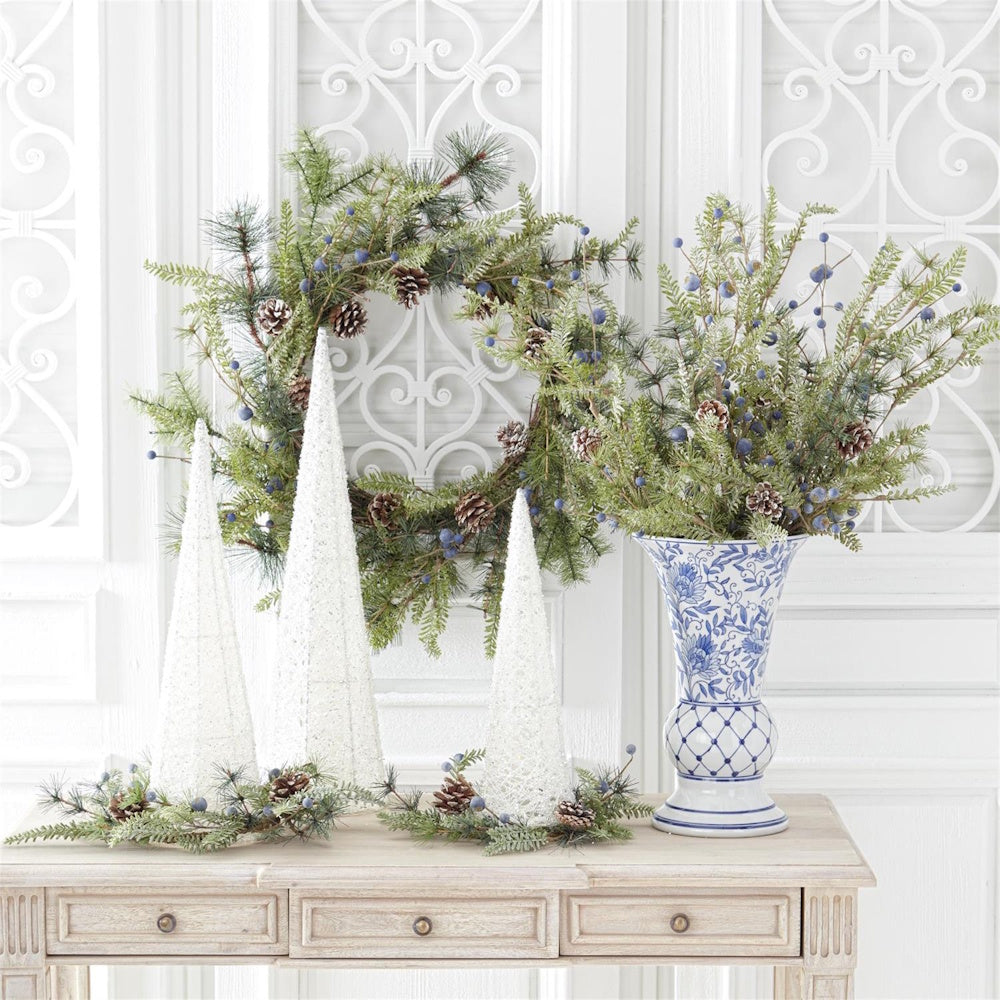Blue and white chinoiserie vase with winter greenery, pinecones, and white cone trees on a wood console table.