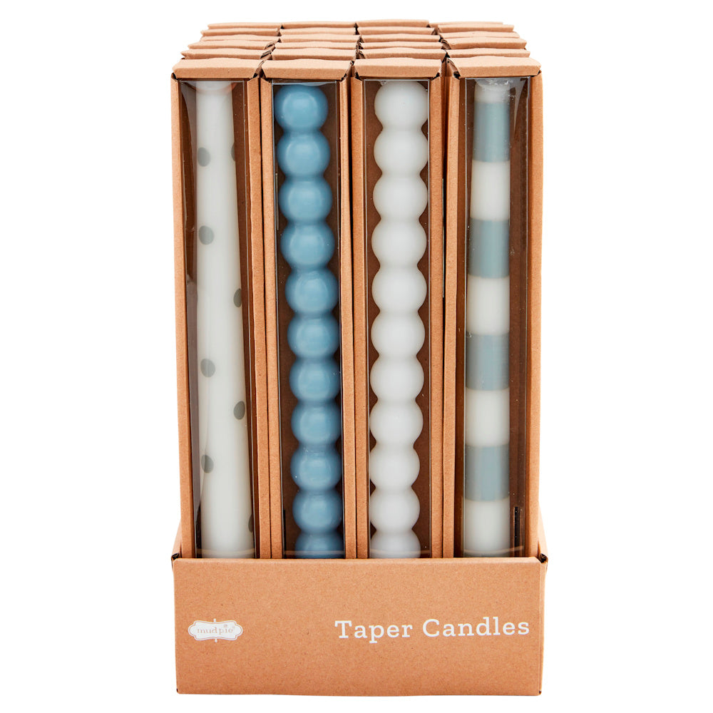 Blue and white patterned taper candles in a cardboard display box, featuring polka dots, stripes, and bubble textures.