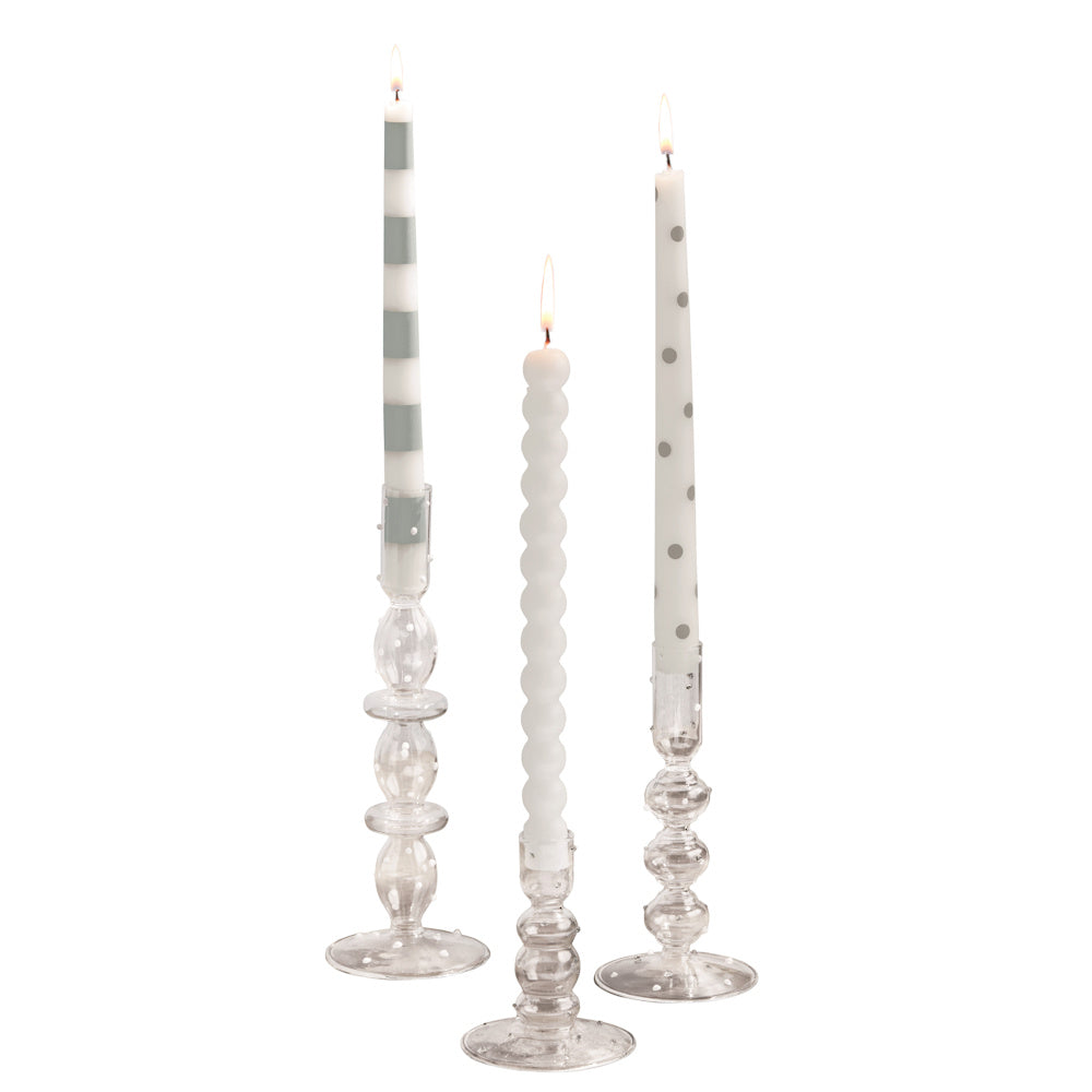 Three lit taper candles in blue and white patterns on clear glass holders, simple and direct decorative home lighting.