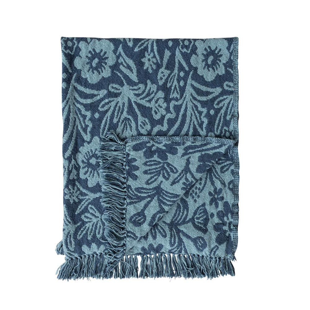 Folded woven recycled cotton blend jacquard throw in blue with a floral pattern and fringed edges.