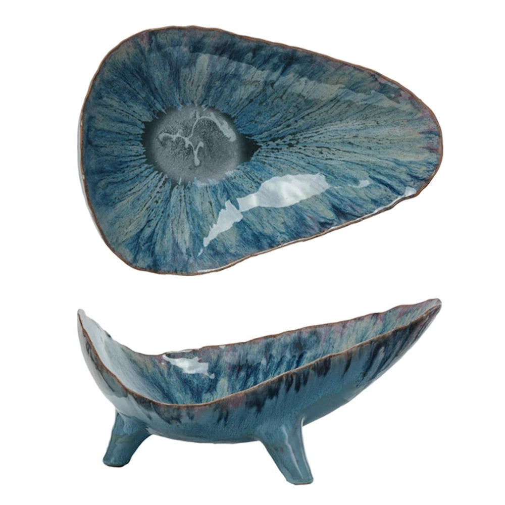 Blue organic-shaped footed stoneware bowl with reactive blue glaze and textured iris-like pattern on a white background.