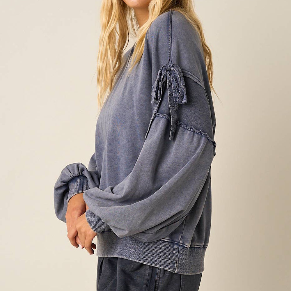Side view of a blue mineral washed cotton sweatshirt with long balloon sleeves and bow details.