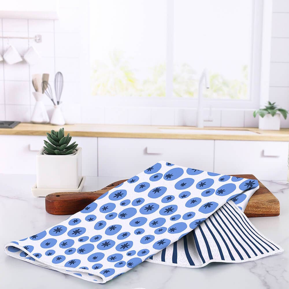 Blueberry-patterned and striped kitchen towels resting on a wooden cutting board on a kitchen counter.