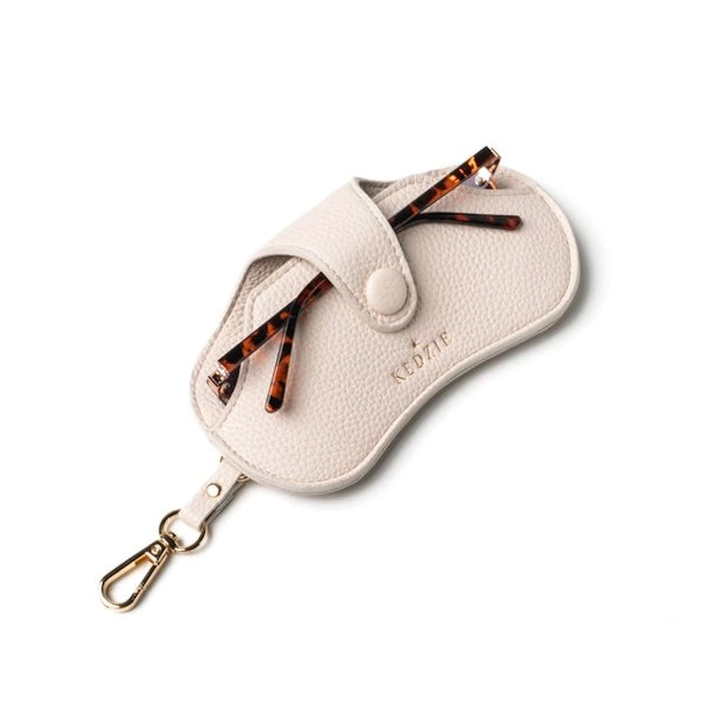 Cream-colored pebbled leather Kedzie eclipse eyewear case with tortoise shell glasses inside and a gold lobster clip.