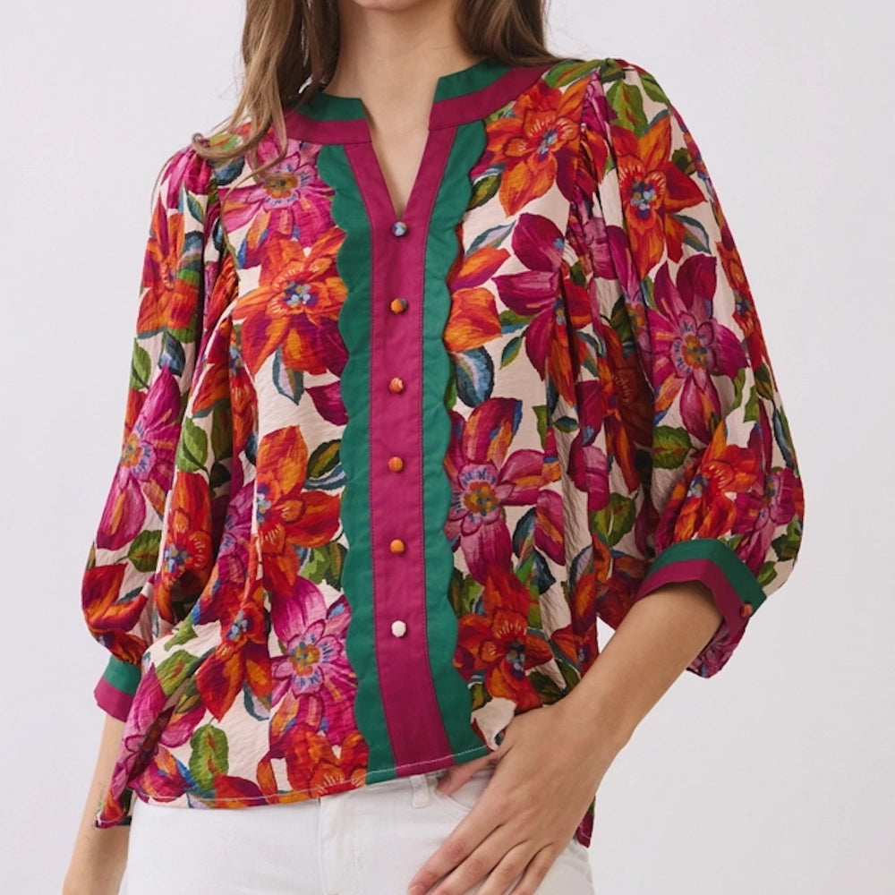Vibrant floral print blouse with scalloped green trim, magenta button placket, and puff sleeves.