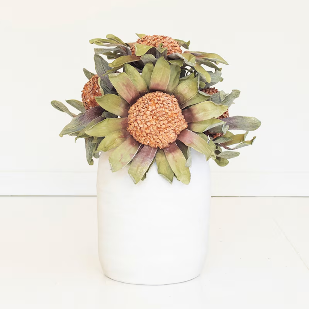 Bouquet of artificial orange protea stems arranged inside a matte white ceramic vase.