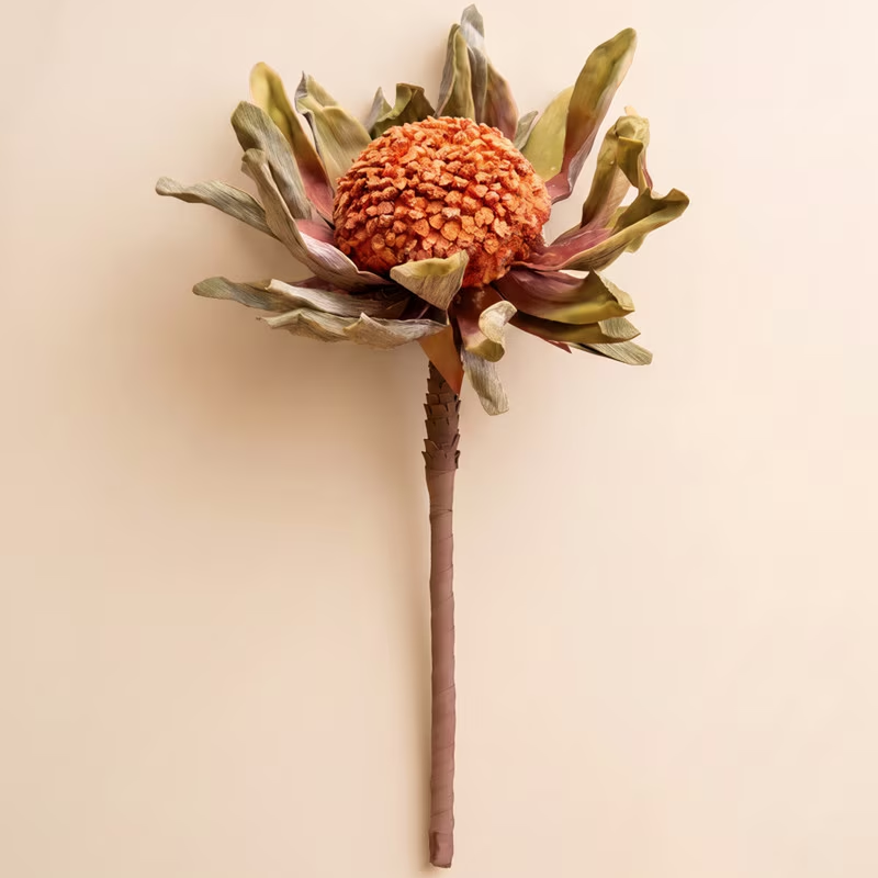 Artificial orange protea stem with spread leafy petals displayed on a light cream background.
