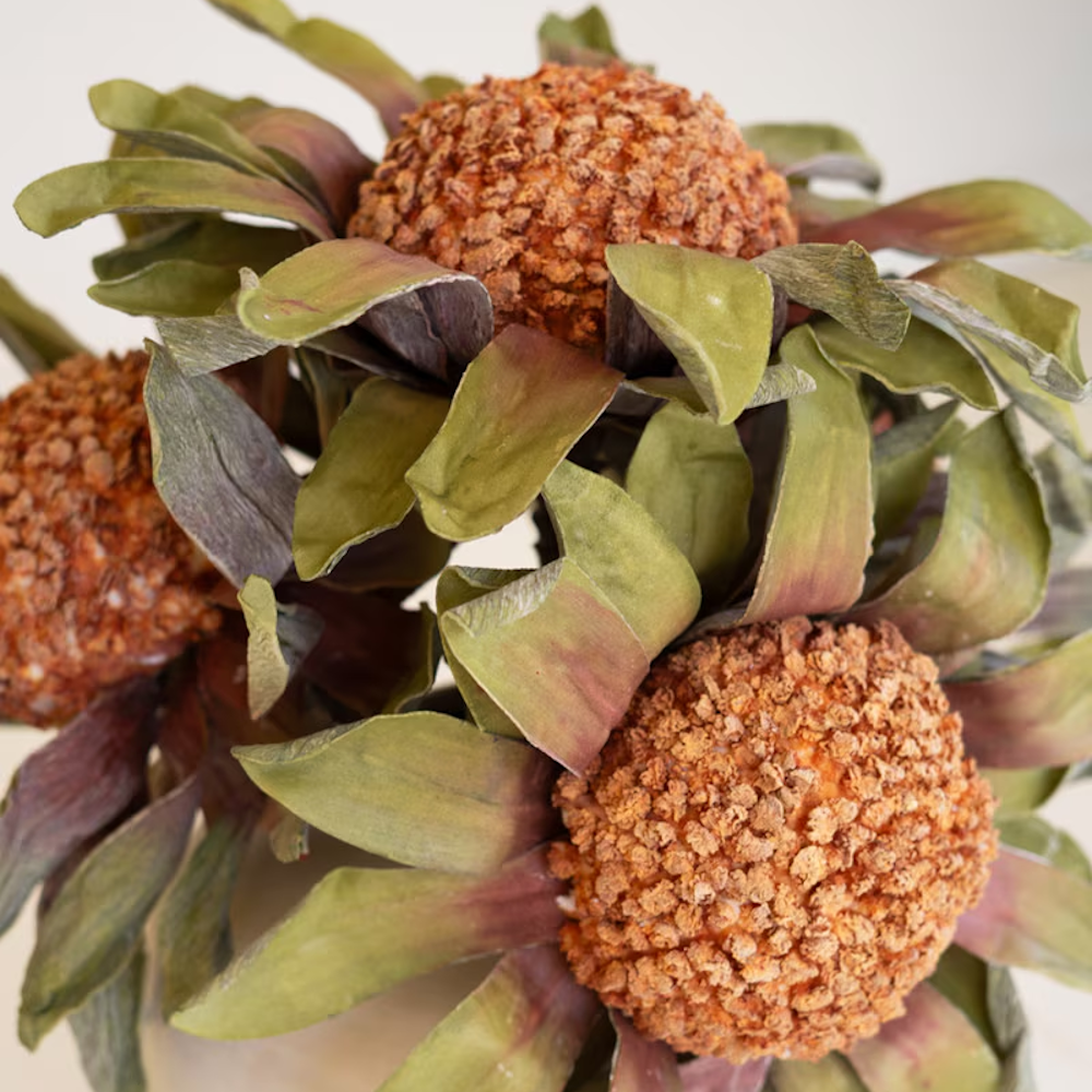 Close-up of textured orange floral heads and muted green leaves on artificial protea stems.