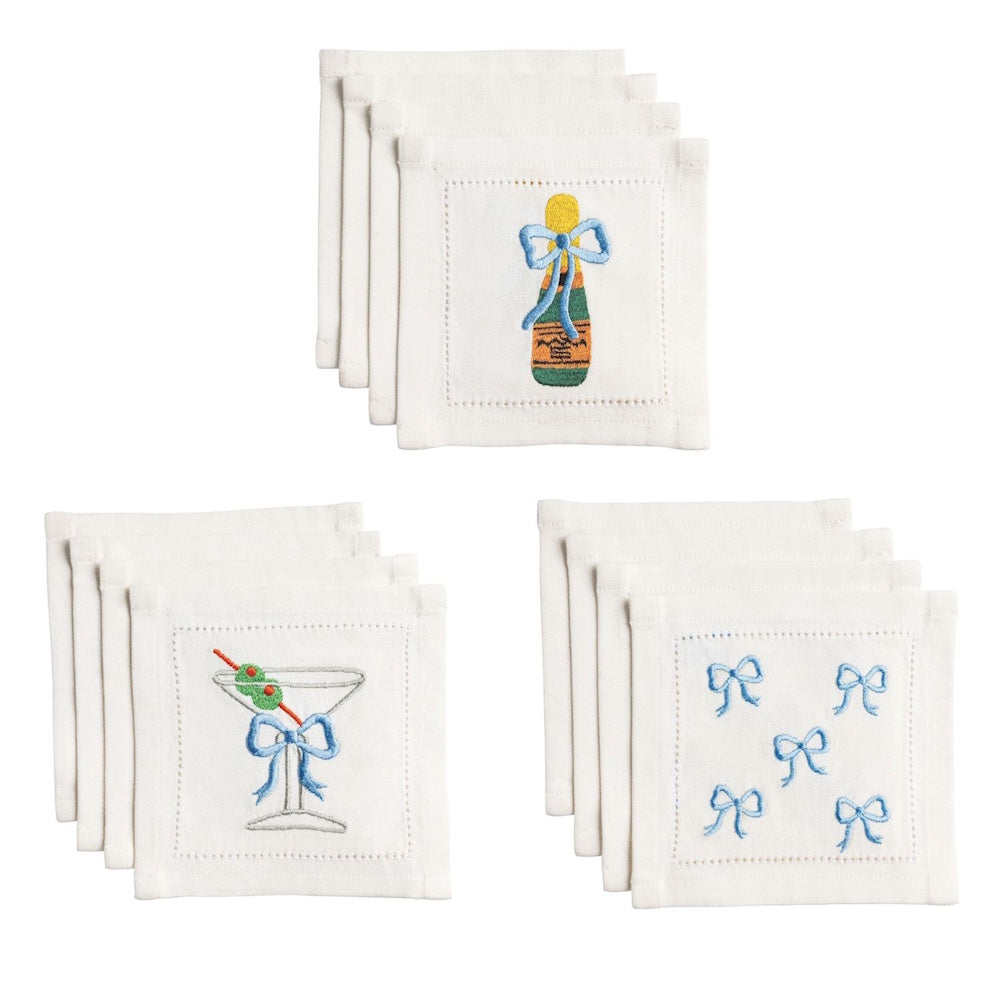 Embroidered white cocktail napkins with blue bows, champagne bottles, martini glasses with olives, and bow patterns.