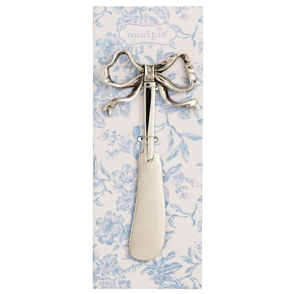 Silver cheese spreader with a vintage bow handle, displayed on a blue floral Mud Pie brand card.