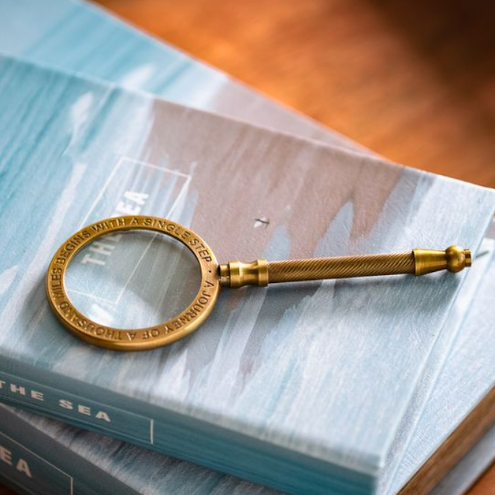 Brass magnifying glass with an engraved metallic rim resting on blue books.
