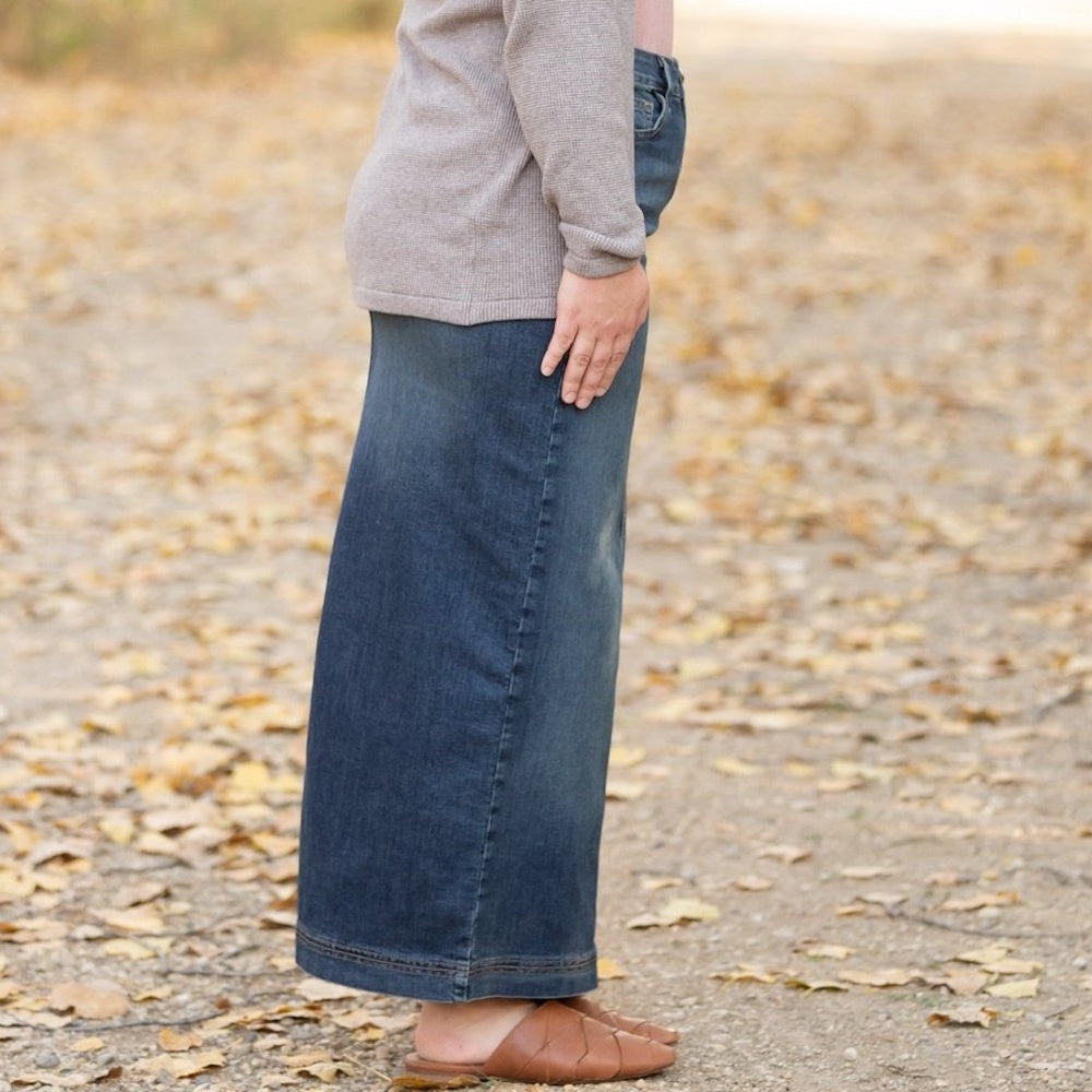Side profile of a person wearing a long denim maxi skirt, a grey cardigan, and brown mule sandals.