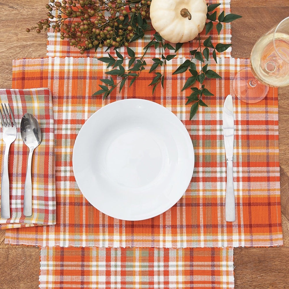 Orange and white plaid table setting with a place mat, white plate, utensils, and mini white pumpkin decor.