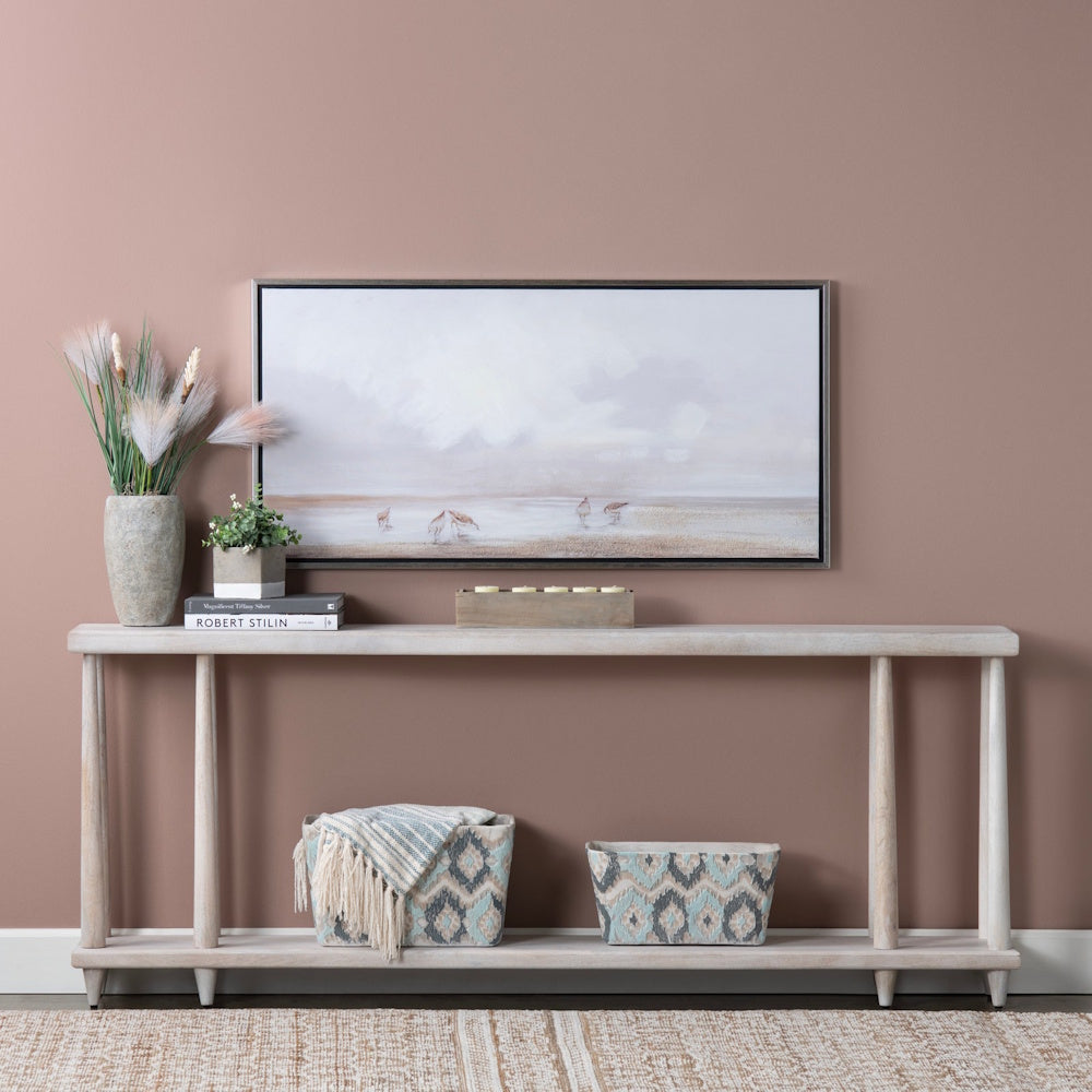 Modern entryway console table with coastal landscape art, decorative baskets, and pampas grass on a dusty rose wall.