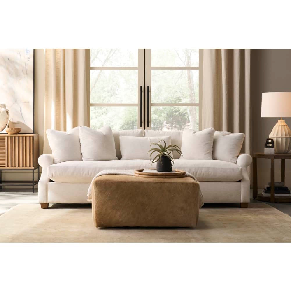 Cream fabric Bristol sofa paired with a tan leather ottoman in a bright, modern living room.
