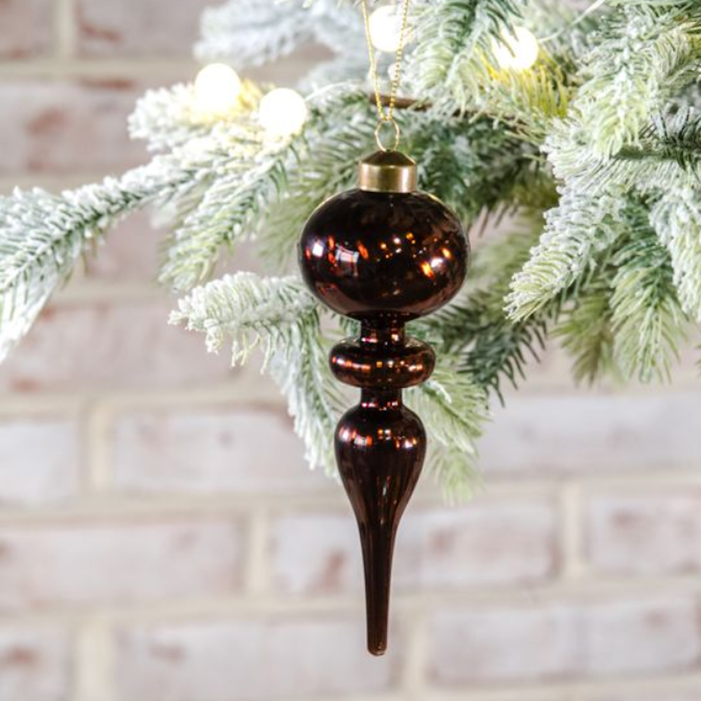 Shiny dark bronze glass finial ornament hanging from a frosted pine branch.