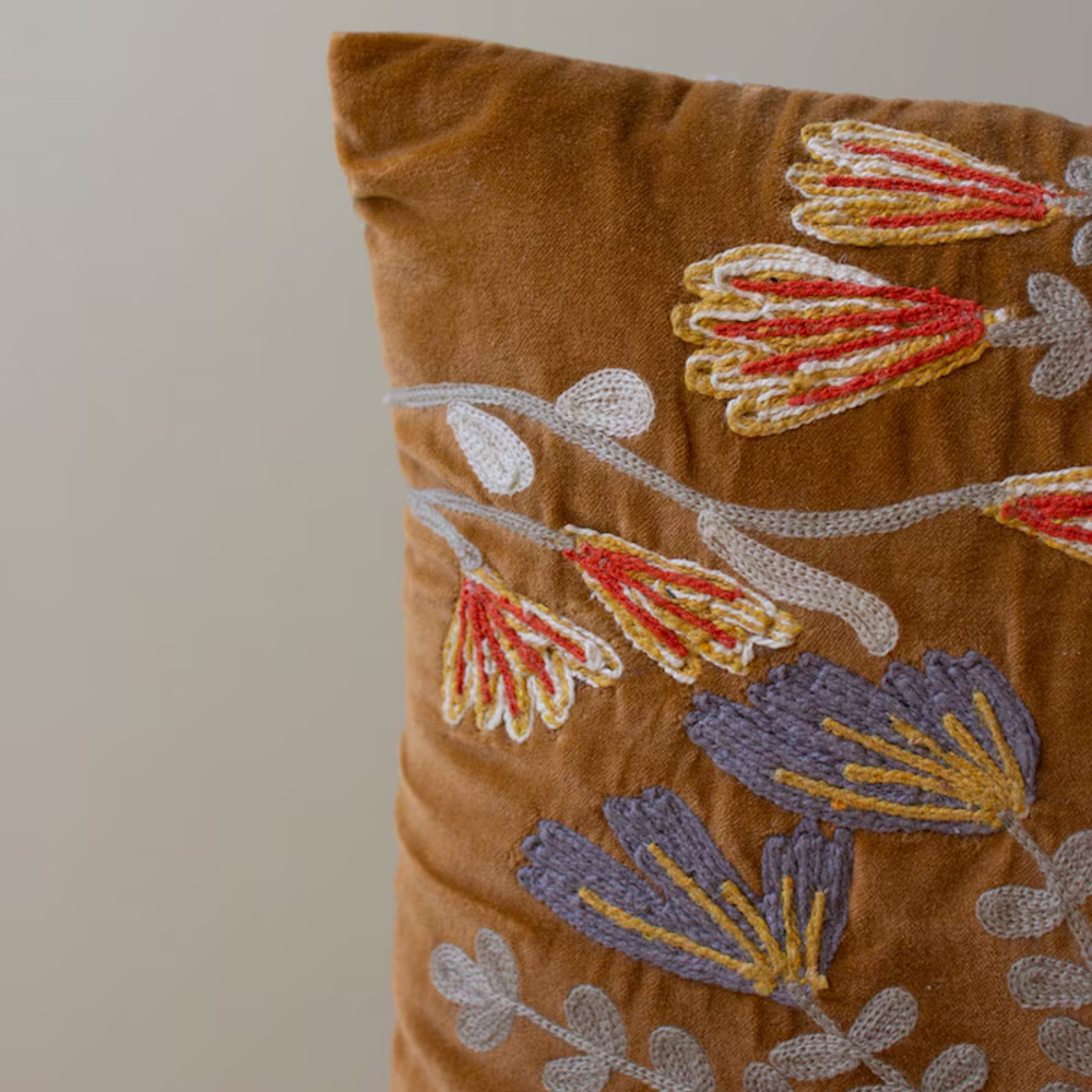 Close-up of a brown velvet pillow featuring detailed floral and leaf embroidery in warm tones.