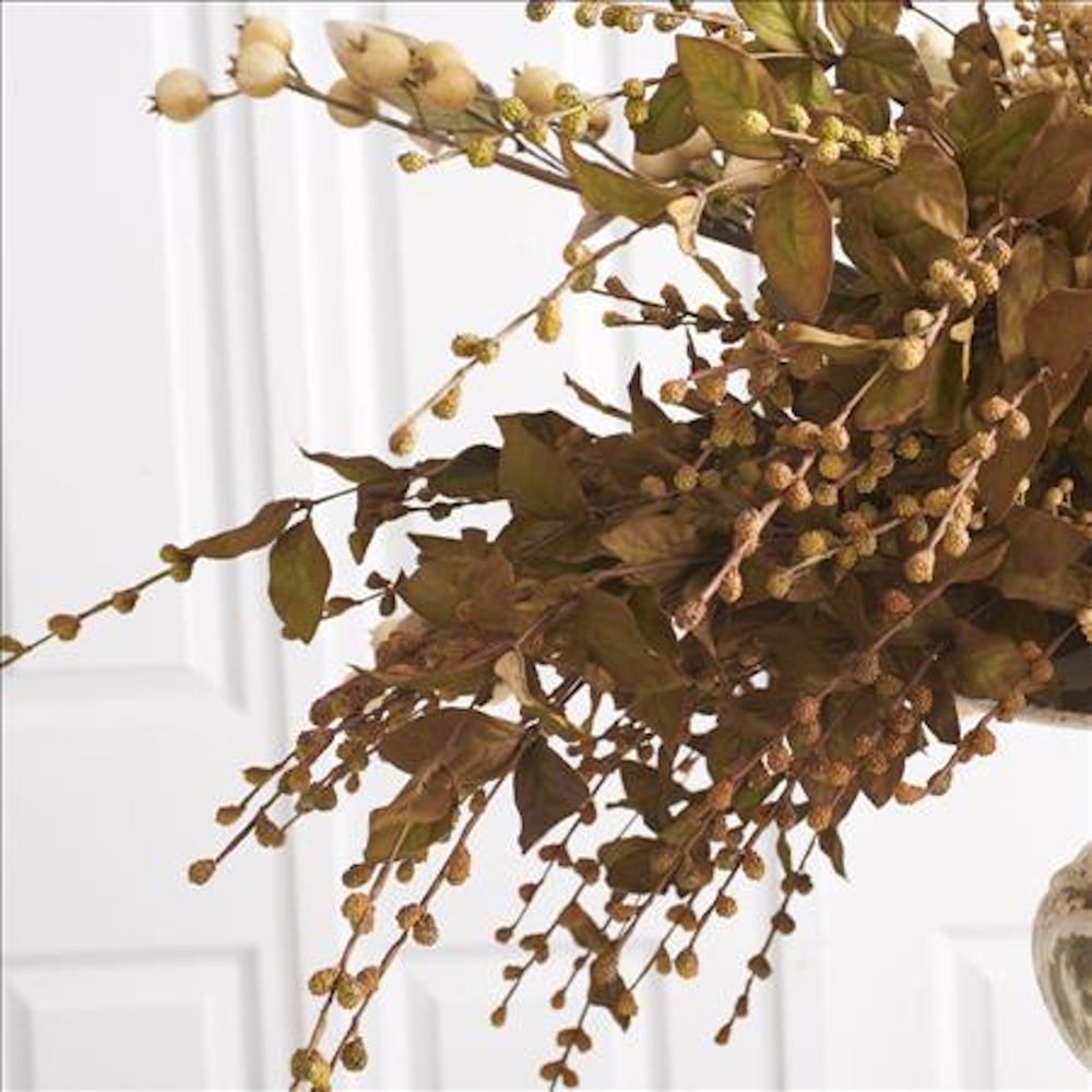 Dried botanical arrangement with brown leaves and small textured berries against a white paneled door.