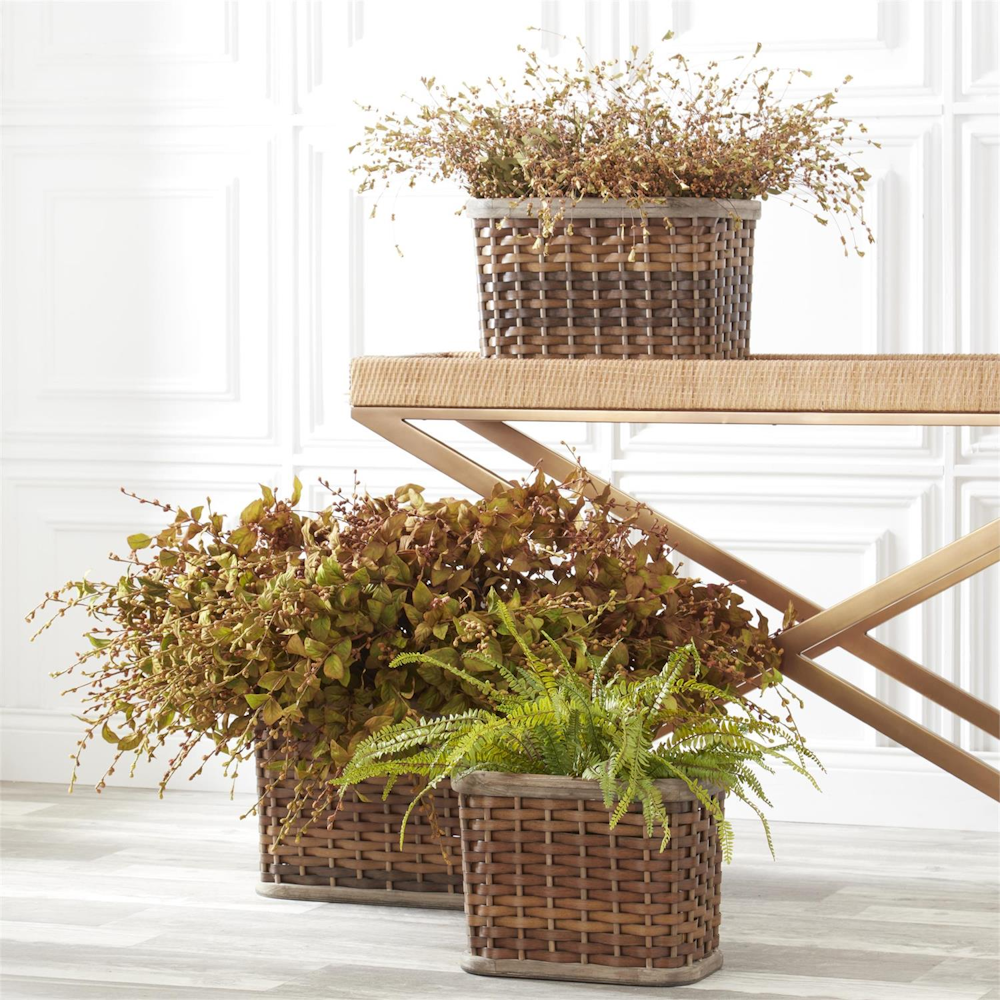 Potted plants and dried botanical arrangements in woven baskets arranged around a gold console table.