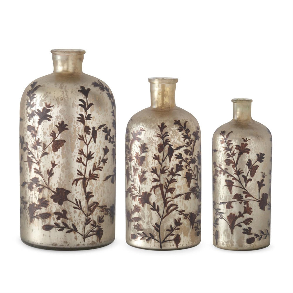 Three champagne mercury glass bottles in graduated sizes, featuring a dark brown floral and vine pattern.
