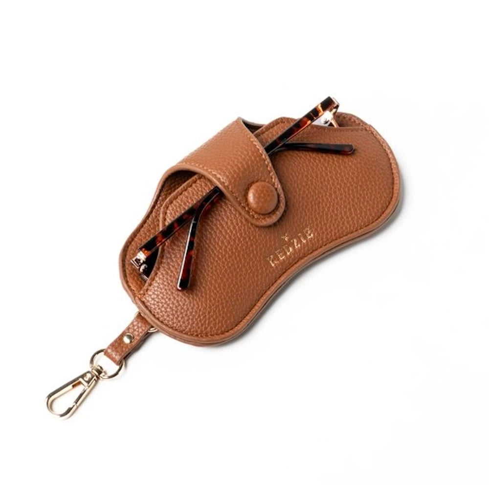 Brown pebbled leather Kedzie eclipse eyewear case with tortoise sunglasses and gold swivel clip on white background.