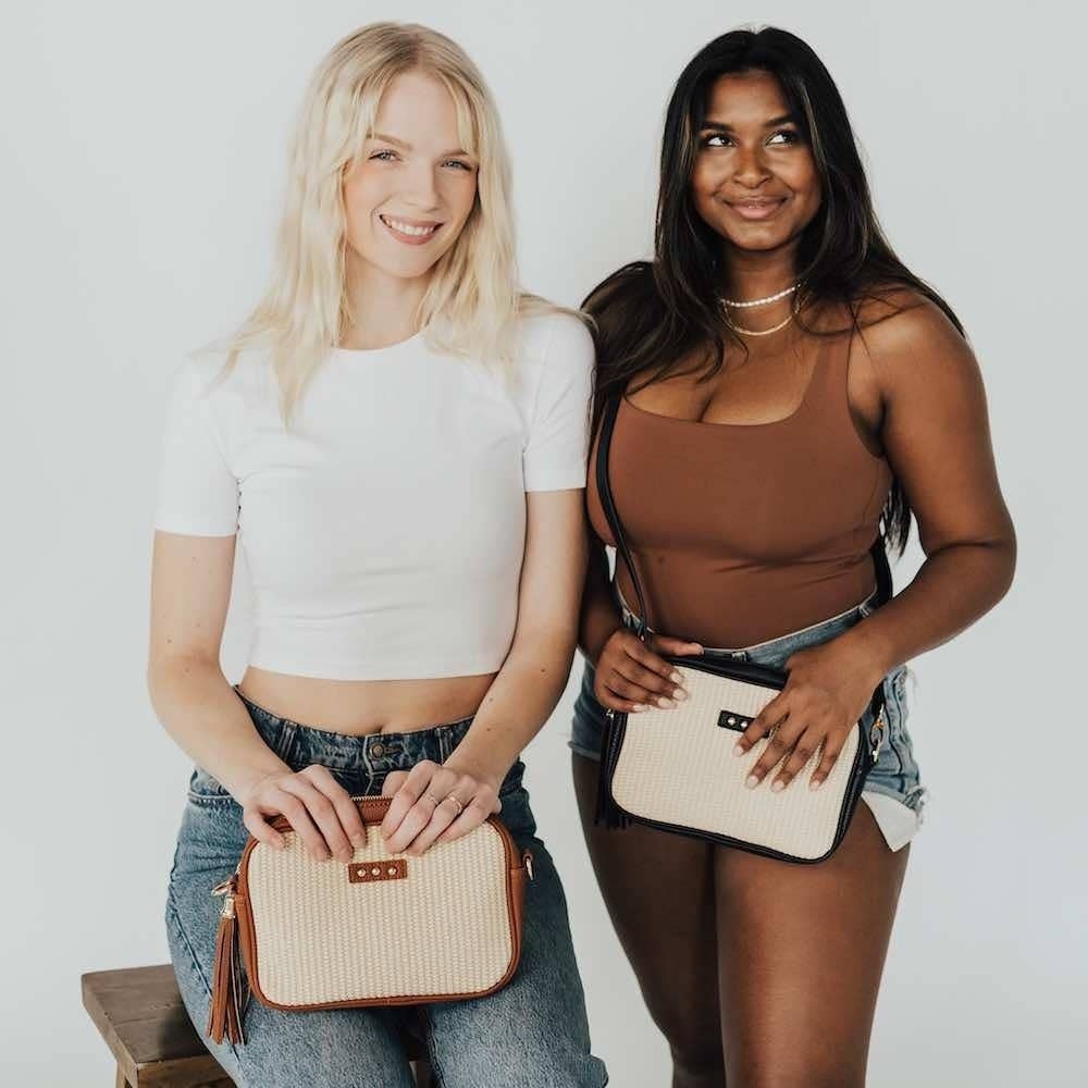 Two women posing together against a white background, each holding a woven crossbody purse.